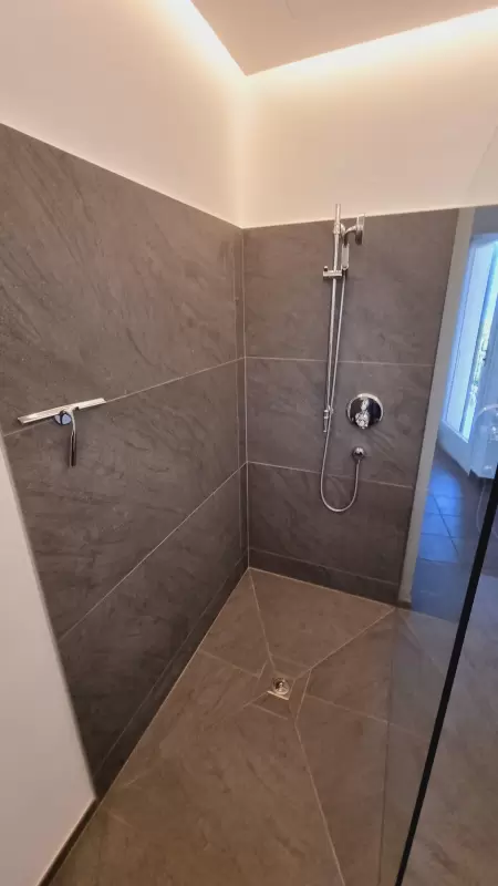 Eine grosszügige, offene Dusche verleiht Ihrem Badezimmer einen charmanten und natürlichen Stil. Das Bild zeigt die ganze Dusche mit Glasduschwand