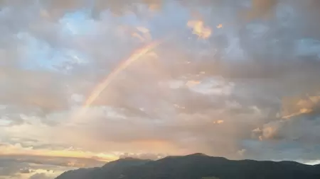 Zu sehen ist ein Regenbogen sder sich uber den Lago Maggiore spannt, er reflektiert im stillen, blau-grünen Wasser. Die Häuser von Brissago. Die Aussicht vom Casa Ramerino erstreckt sich fast über den ganzen Lago Maggiore.