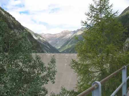 Tauchen Sie ein in die mystische Welt der Verzasca Staumauer und lassen Sie sich von ihrer geheimnisvollen Aura verzaubern. Das Bild zeigt zwischen de Bäumen die Staumauer.