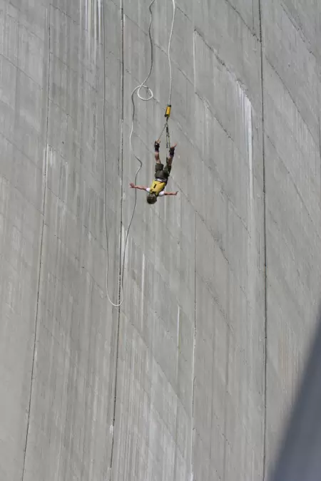 Erleben Sie den ultimativen Nervenkitzel beim Bungee-Jumping im Verzascatal, wo Sie sich frei wie ein Vogel fühlen können. Das Bild zeigt eine Pererson im freiehn Fall an der Staumauer entlang am Bungee-Jumpingseil